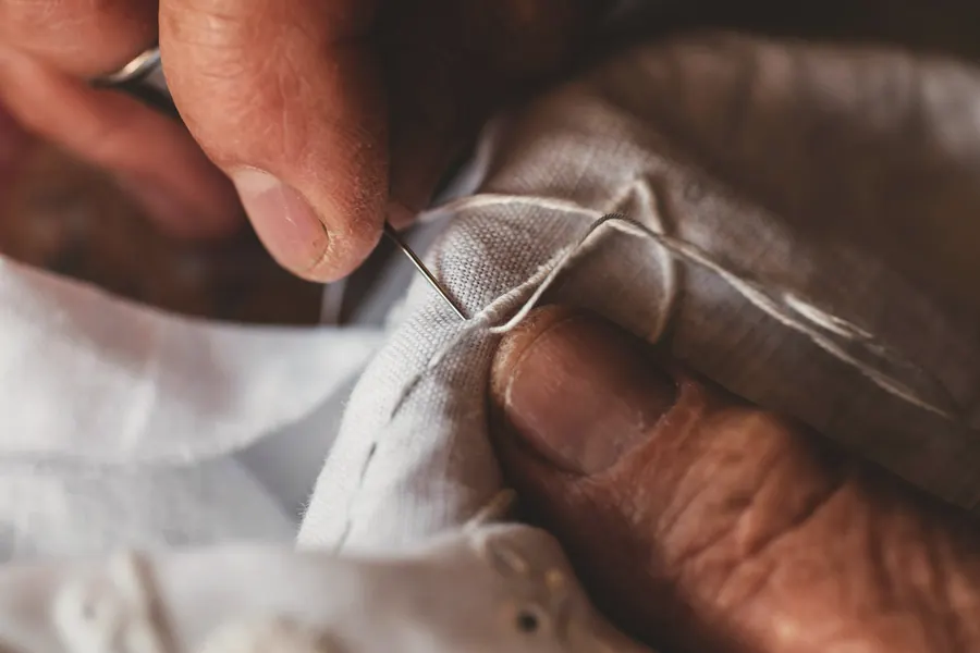 Hands sewing white fabric with a needle and thread